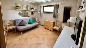 A compact room with a sofa bed, a small wooden dresser, a TV, and a window with curtains. - Short periods Reggio Emilia center  (Reggio Emilia)