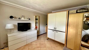A room with a TV on a white cabinet, a wooden wardrobe, and a shelf with decorative items. - Short periods Reggio Emilia center  (Reggio Emilia)
