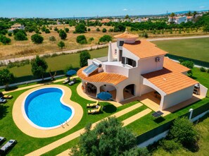 A large house with a swimming pool, multiple lounge chairs, and a well-maintained lawn.
