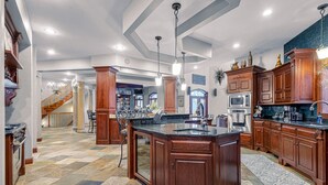 Una cocina amplia con una isla grande, armarios de madera y piso de baldosas de piedra.