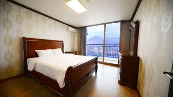 A bedroom with a large bed, a wooden dresser, and a balcony with a mountain view.