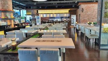 Une cafétéria spacieuse avec de nombreuses tables et chaises, un mur en briques et une cuisine moderne en arrière-plan.