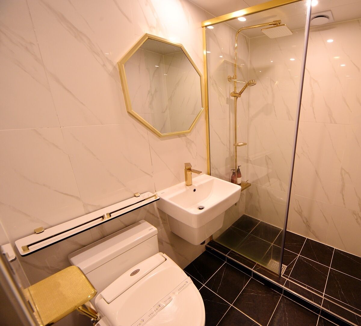 A bathroom with a white sink, a toilet, a glass shower enclosure, and a marble-tiled floor.