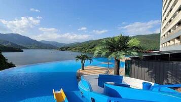 A swimming pool with a water slide, palm trees, and a view of mountains.