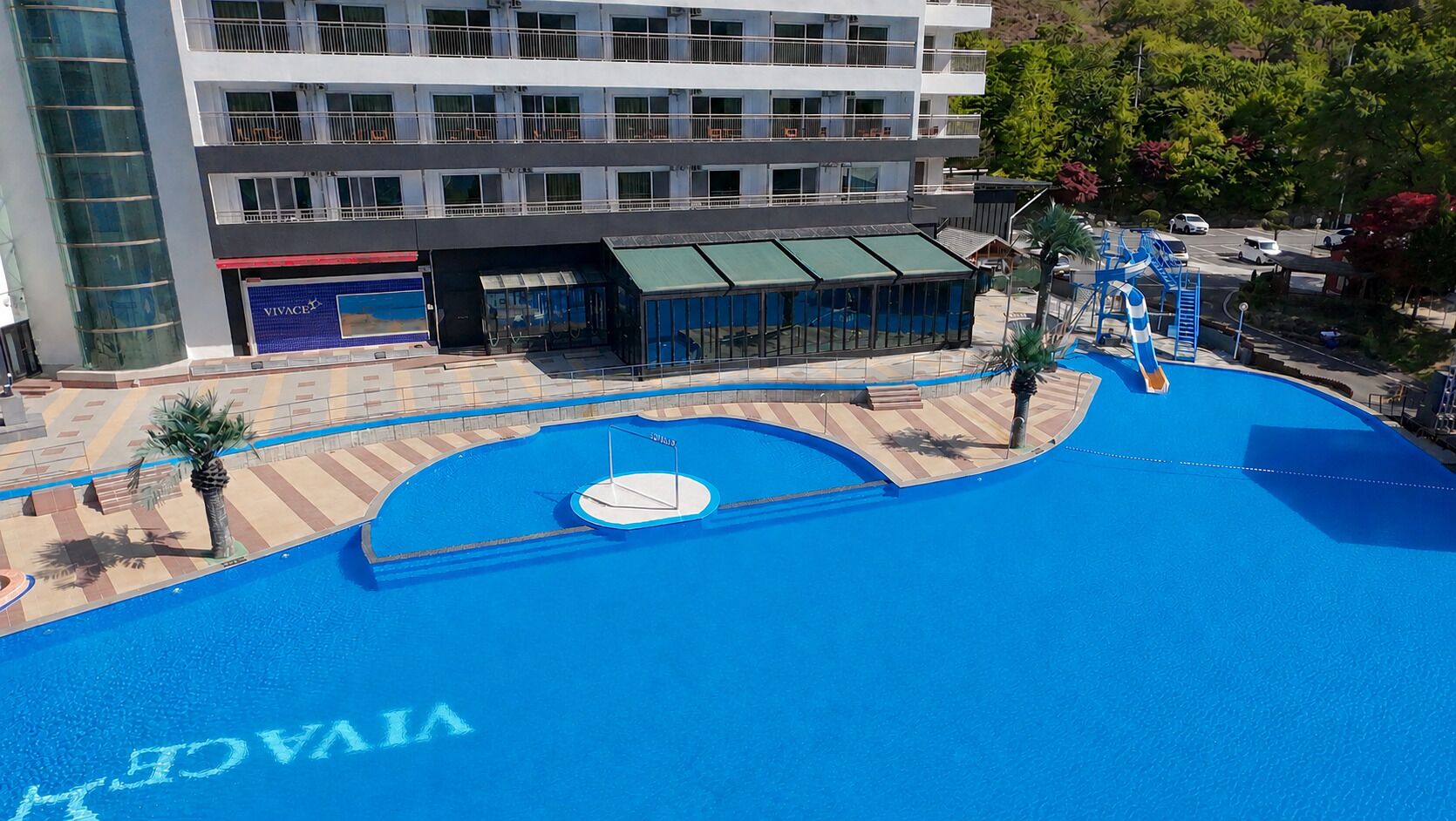 Un hotel con piscina, zona cubierta y un edificio con balcones.
