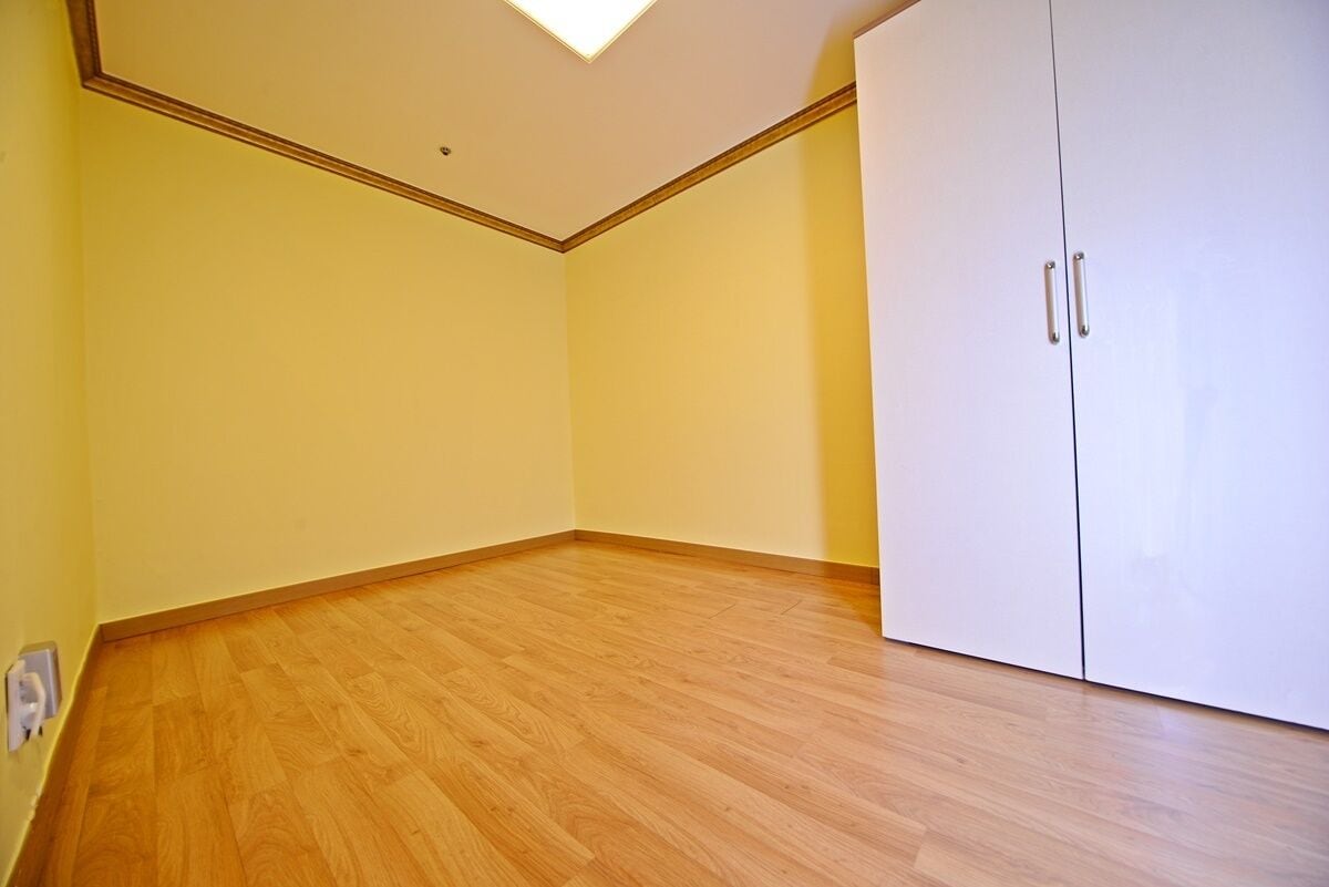 A room with wooden flooring, a white wardrobe, and a ceiling light fixture.