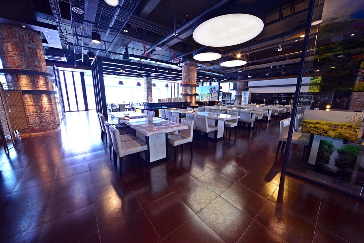 Un interno ristorante moderno con soffitti alti, pareti in mattoni a vista e diverse disposizioni di posti a sedere, tra cui tavoli e banconi.