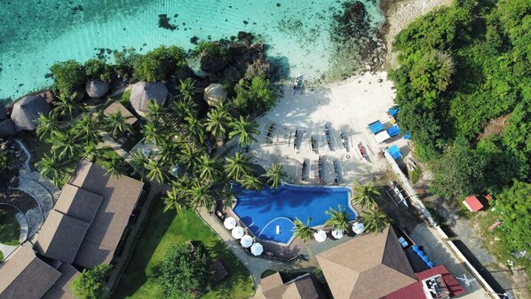 Ein Luftbild eines Resorts mit Schwimmbad, Strandbereich und üppiger Vegetation.