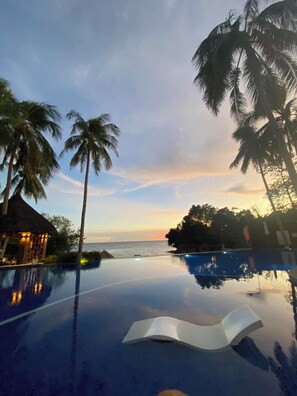 Ein ruhiger Infinity-Pool mit Blick auf das Meer und Palmen bei Sonnenuntergang.