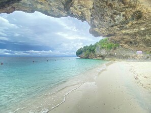 Une plage à l’eau turquoise et limpide, un rivage sablonneux et une falaise rocheuse couverte de végétation.