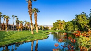 A golf course with a pond, palm trees, and a building in the background.