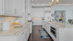 A modern kitchen with white cabinetry, a marble countertop, and a central island. - Ocean View, Gulf Access, Close to Beach, Private heated Pool - Island Waters  - Roelens (Fort Myers Beach)