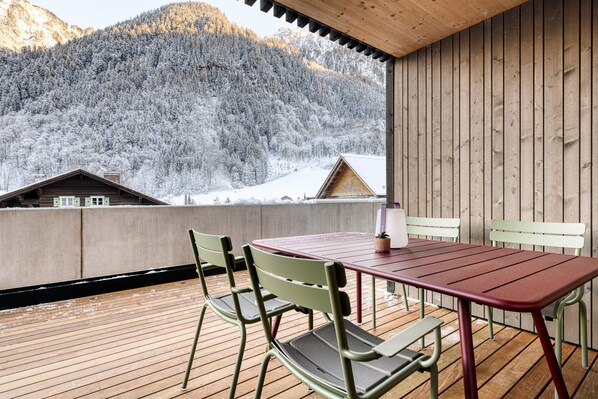 A wooden deck with a table and chairs, overlooking a snowy mountain landscape.