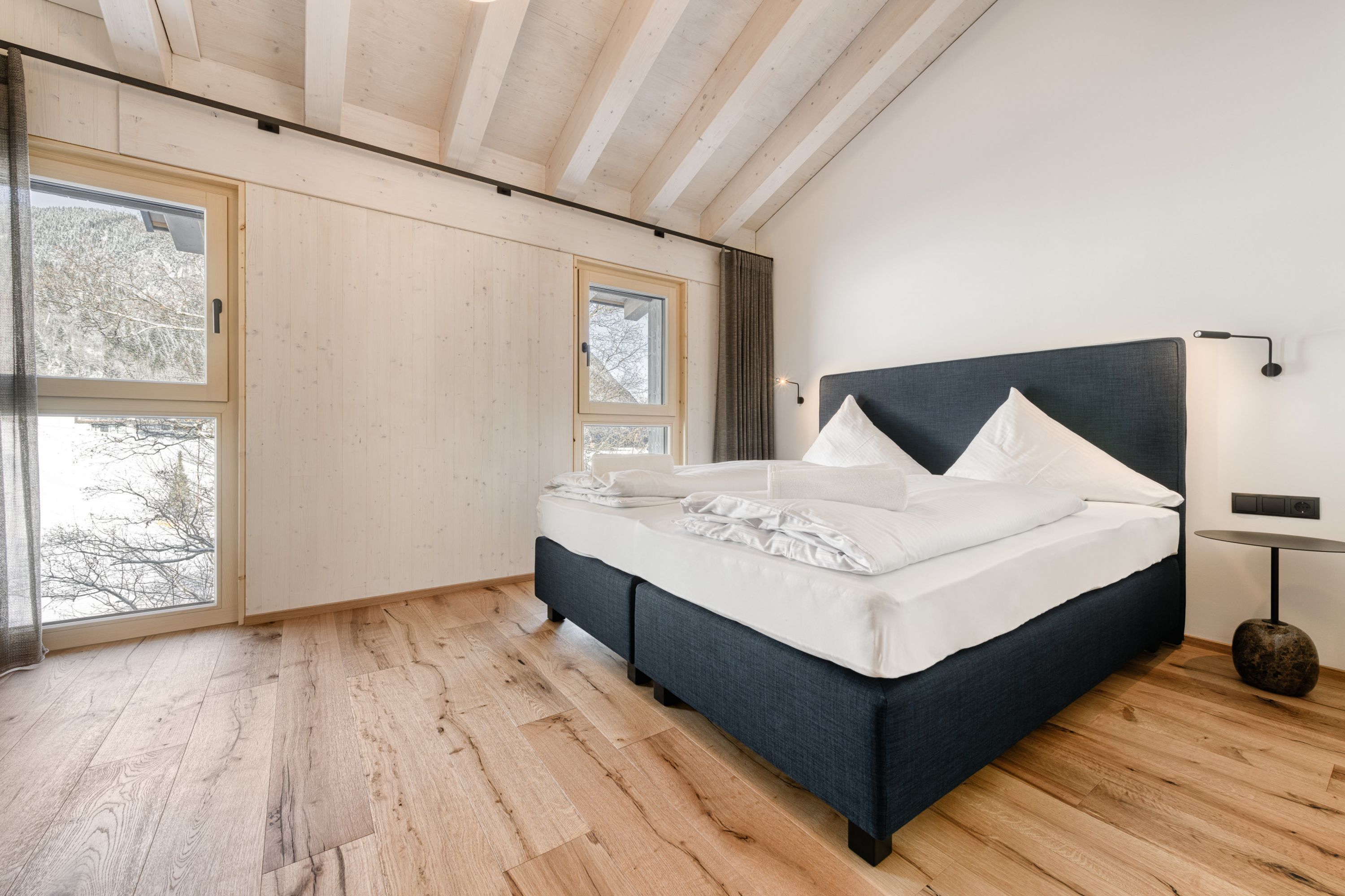 Una camera da letto moderna con un letto grande, pavimento in legno e ampie finestre.