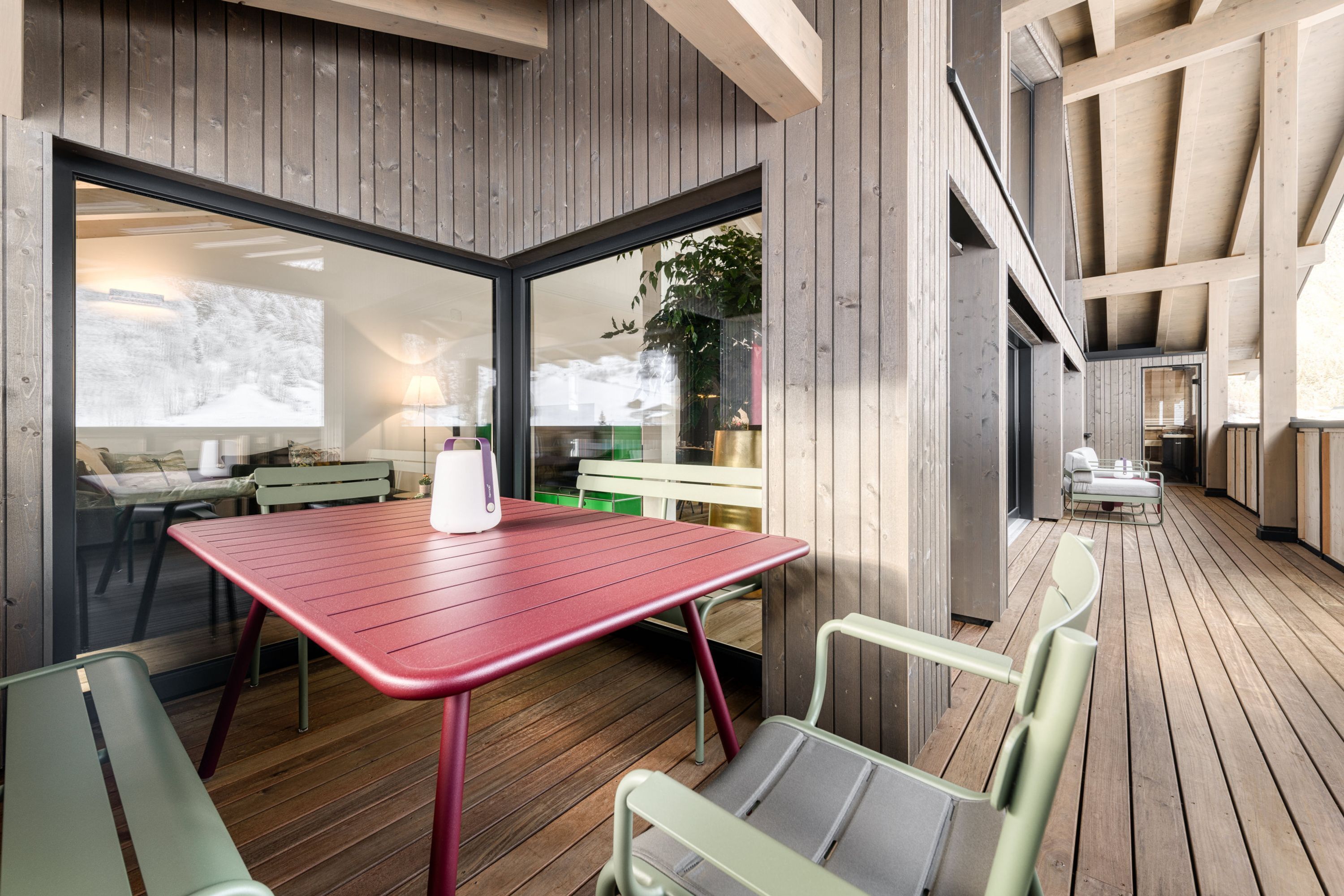 A wooden deck with a red table and chairs, a sofa, and a bench.