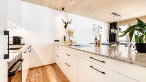A modern kitchen with white cabinetry, a wooden ceiling, and a large island with a sink. - Ferienwohnung Family Zentral (Brand)