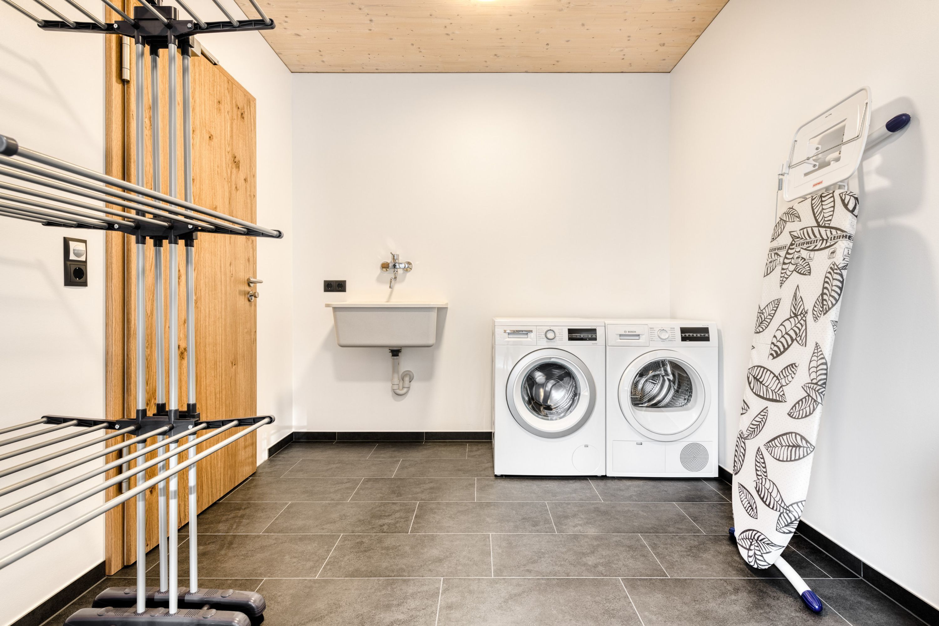 Een wasruimte met een droogrek, wasmachine en gootsteen.