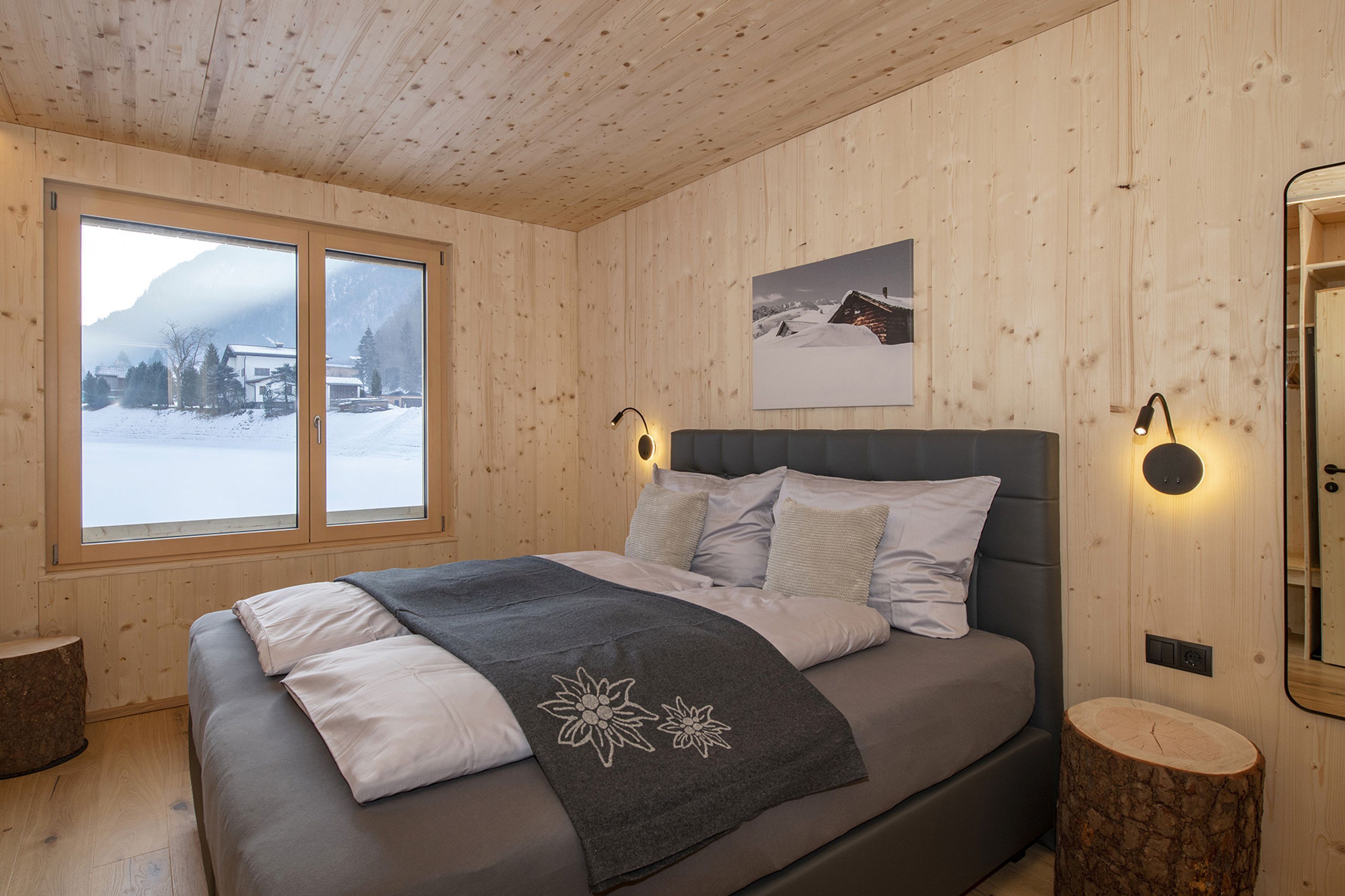 A wooden-paneled bedroom with a bed, a window with a snowy view, and a wall-mounted picture.