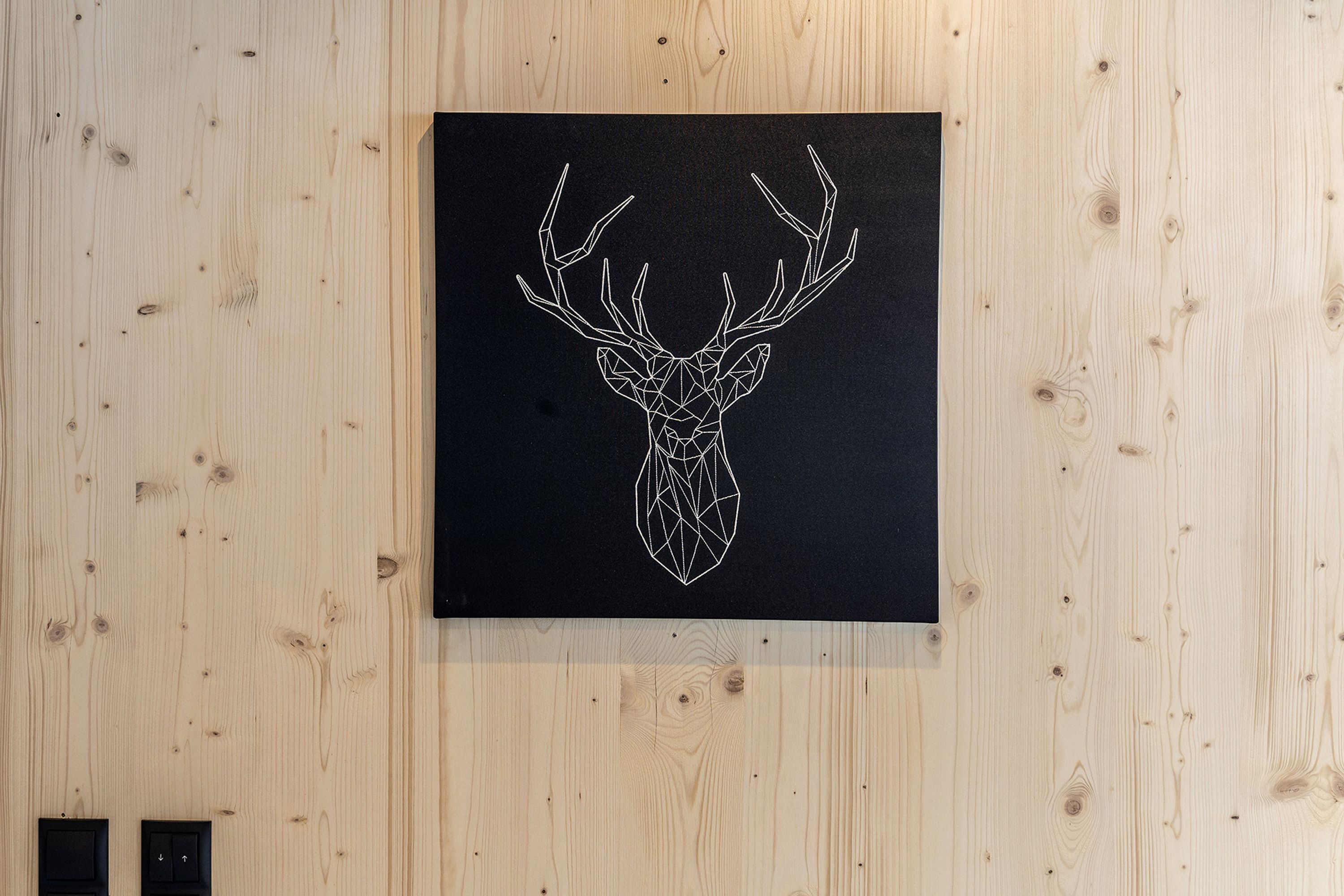 A geometric deer head artwork on a black background, mounted on a wooden wall.