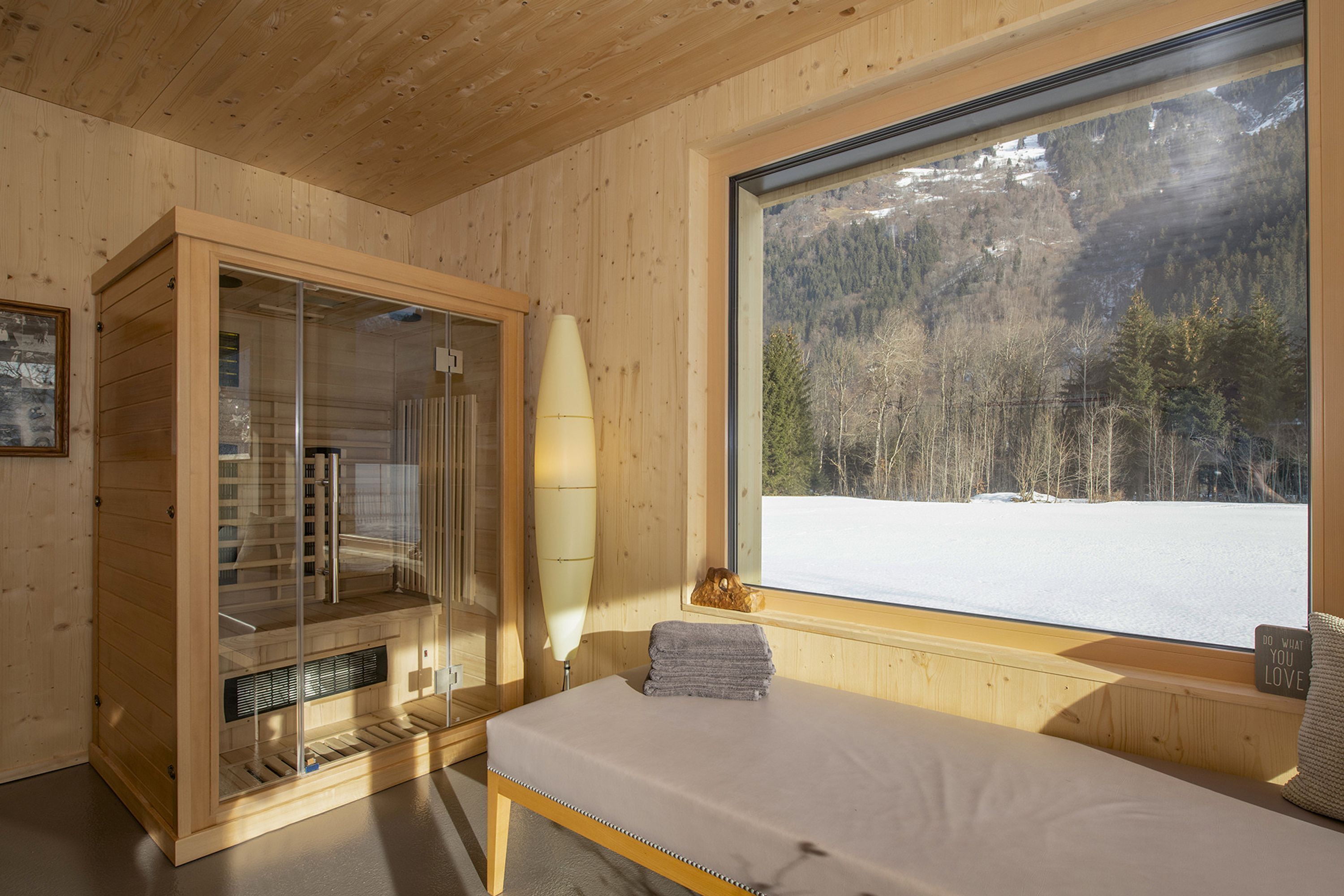 A wooden cabin room with a bed, a glass shower enclosure, and a large window with a snowy mountain view.