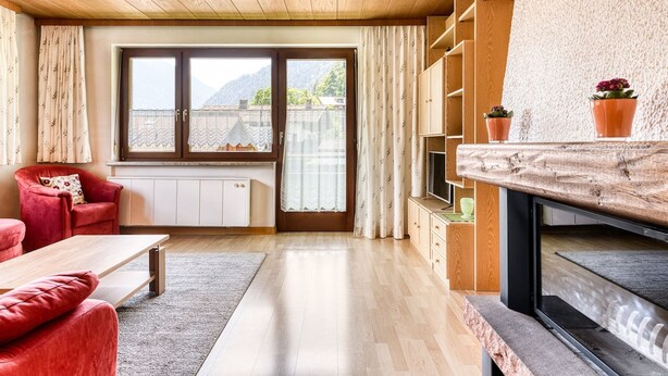 A modern living room with a wooden ceiling, a large window with a view of mountains, a red sofa, a wooden coffee table, and a TV on a wooden stand. - Appartement Sassella - M Ser-apartments (Tschagguns)