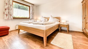 A bedroom with a wooden bed, a nightstand, a red chair, and a window with floral curtains. - Appartement Sassella - M Ser-apartments (Tschagguns)