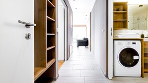 A narrow hallway with a wooden wardrobe, a washing machine, and a glimpse of a bathroom with a mirror and shelves. - Appartement Panorama Blick (Buerserberg)
