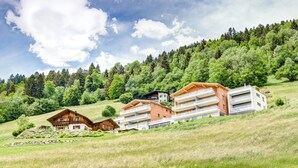 A hillside with a row of wooden cabins and a modern building with balconies. - Appartement Panorama Blick (Buerserberg)