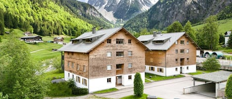 A multi-story building with a brick facade, a parking area, and a view of a mountainous landscape.