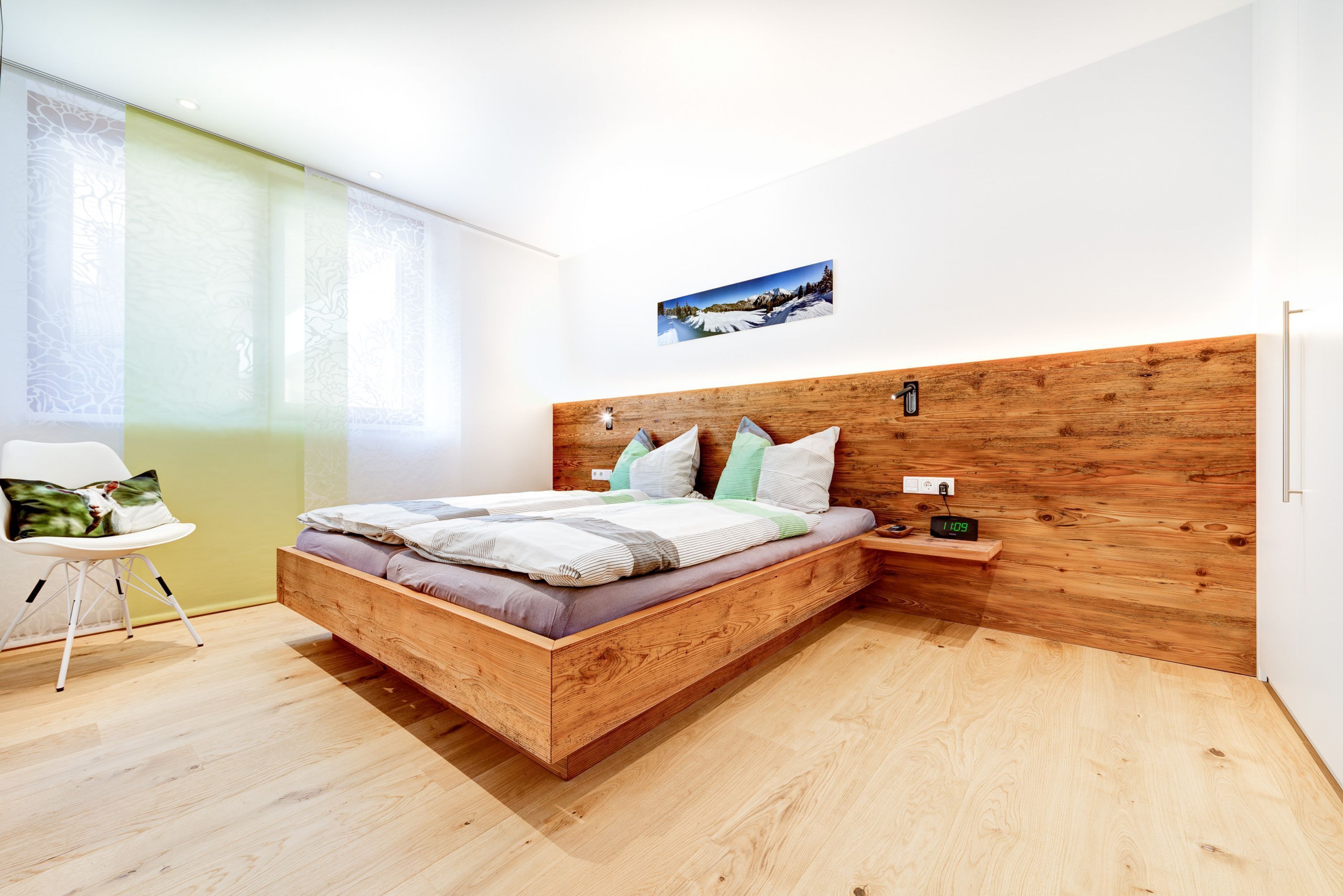 A modern bedroom with a wooden bed frame, a bedside table, and a wall-mounted clock.