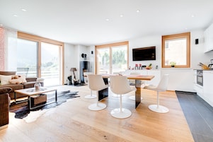 Un salón moderno con un ventanal grande, una chimenea y un comedor con sillas blancas.