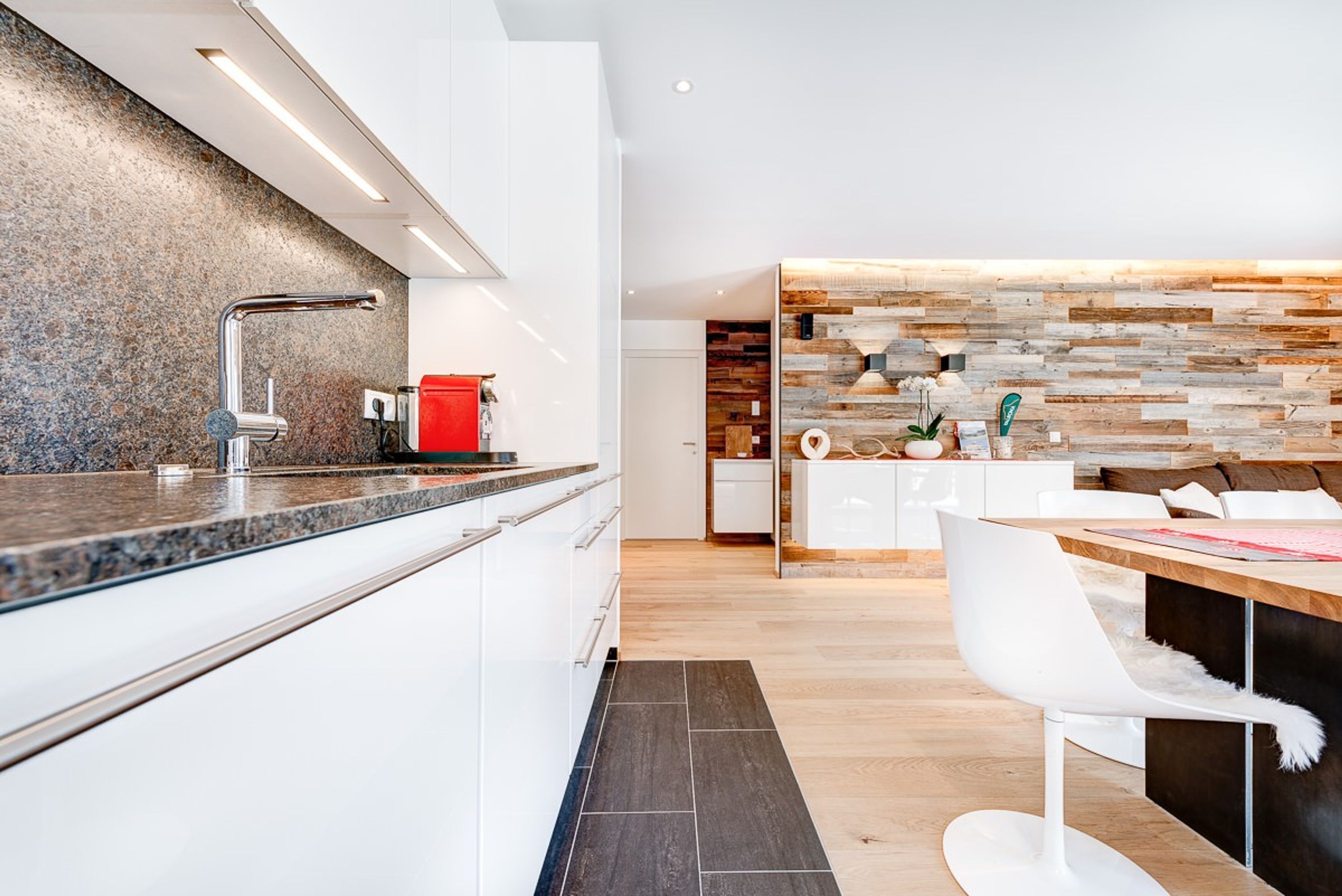 A modern kitchen with a granite countertop, stainless steel faucet, and a red kettle.
