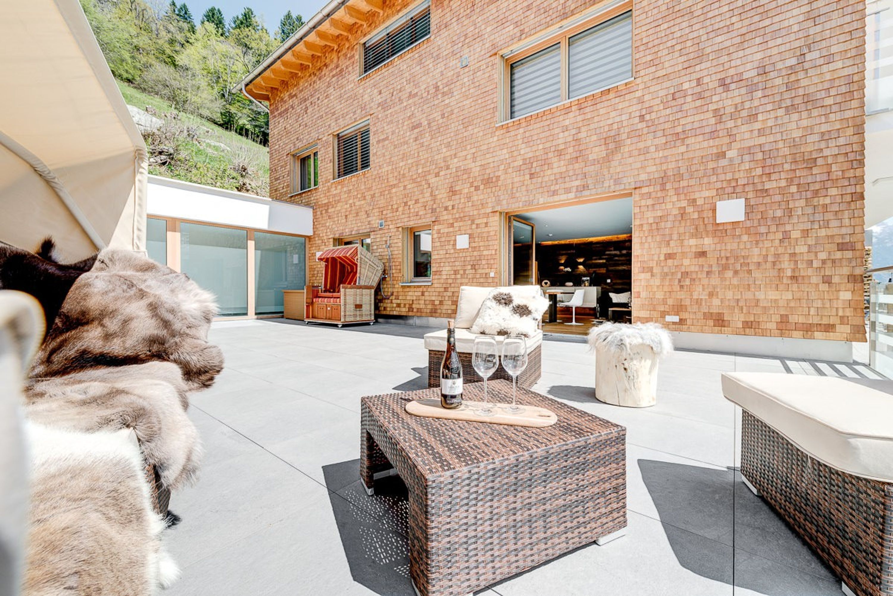 Un patio exterior moderno con pared de ladrillo, mobiliario de mimbre y puerta de cristal que da a una habitación.