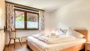 Une chambre avec un lit en bois, une chaise, une fenêtre avec des rideaux et une vue sur la verdure à l’extérieur.