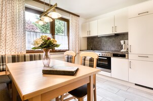 Una cocina moderna con armarios blancos, horno empotrado y un comedor con mesa y sillas de madera.