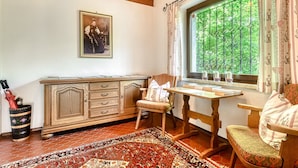 A room with a wooden cabinet, a chair, a table, a patterned rug, and a window with a view of greenery. - Appartement Golm - M Ser-apartments (Tschagguns)