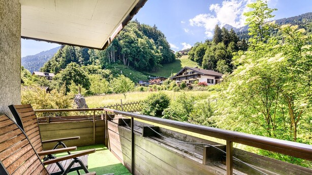 A balcony with wooden chairs, a wooden railing, and a view of a green landscape with houses and trees. - Appartement Golm - M Ser-apartments (Tschagguns)