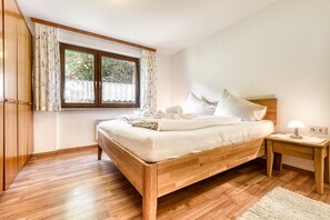 Une chambre à coucher avec un lit en bois, une table de chevet avec une lampe, une fenêtre avec des rideaux et une armoire.