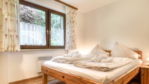 A wooden bed with white linens, a window with floral curtains, and a wooden nightstand. - Appartement Golm - M Ser-apartments (Tschagguns)