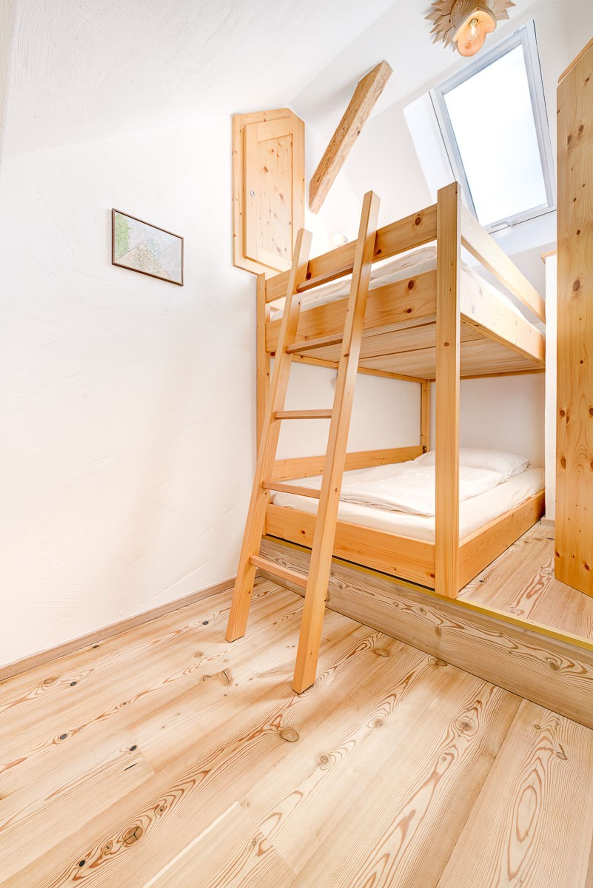 A bunk bed with a wooden ladder, a skylight, and a framed map on the wall.