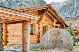 Una cabaña de madera con un letrero de piedra que dice "ANDAM" y una escultura de ciervo de madera.
