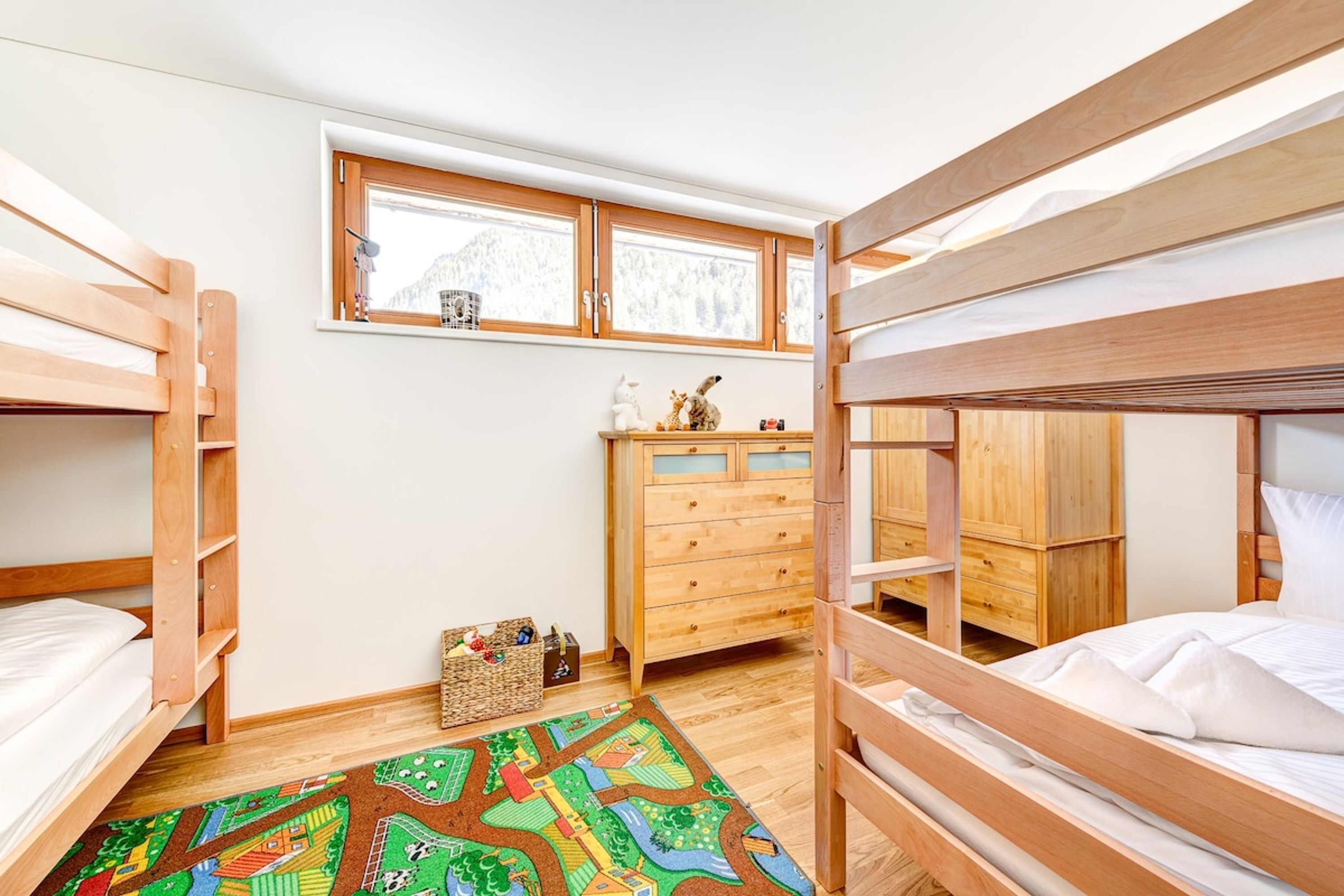 A bunk bed room with a wooden dresser and a window.