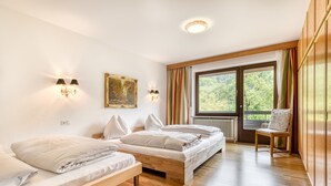 A bedroom with two beds, a wooden floor, a window with curtains, and a chair. - Panoramavilla Bludenz (Bludenz)