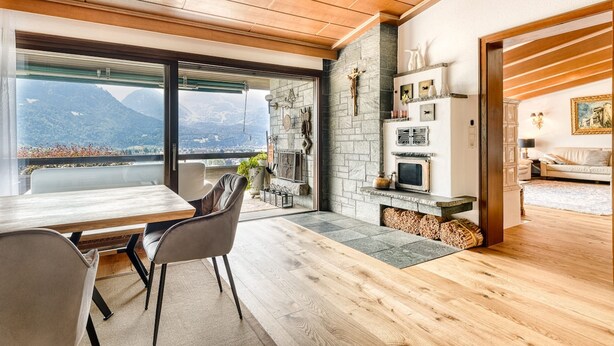A modern living room with a fireplace, a dining area with a table and chairs, and a view of mountains through large windows. - Panoramavilla Bludenz (Bludenz)