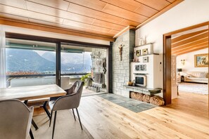 A modern living room with a fireplace, a dining area with a table and chairs, and a view of mountains through large windows. - Panoramavilla Bludenz (Bludenz)