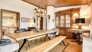 A dining area with a wooden table and chairs, a bench, a chandelier, and a cabinet with glass doors. - Panoramavilla Bludenz (Bludenz)