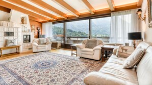 A spacious living room with a large window offering a mountain view, a cozy fireplace, and a plush sofa. - Panoramavilla Bludenz (Bludenz)