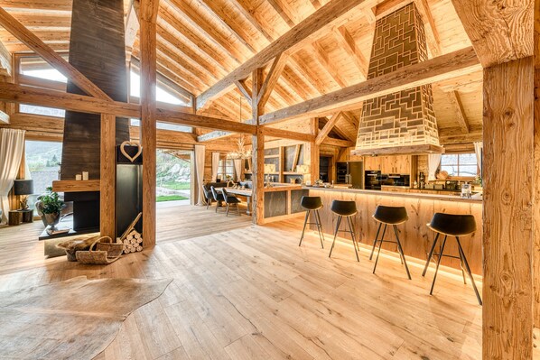A spacious wooden interior with a high ceiling, a central fireplace, and a bar area with stools.