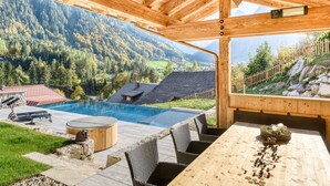Eine Holzterrasse mit Pool, Korbstühlen und einem Tisch mit dekorativer Mittelstück.