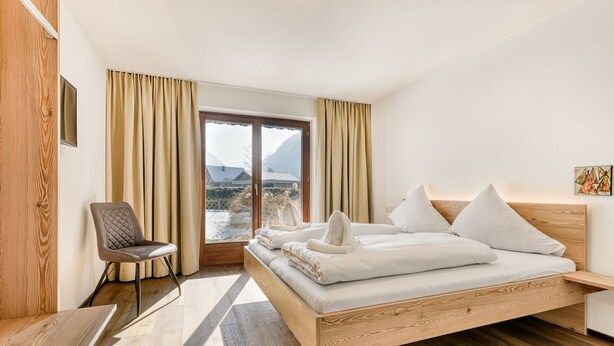 Een moderne slaapkamer met een houten bed, een stoel en uitzicht op bergen door een groot raam.